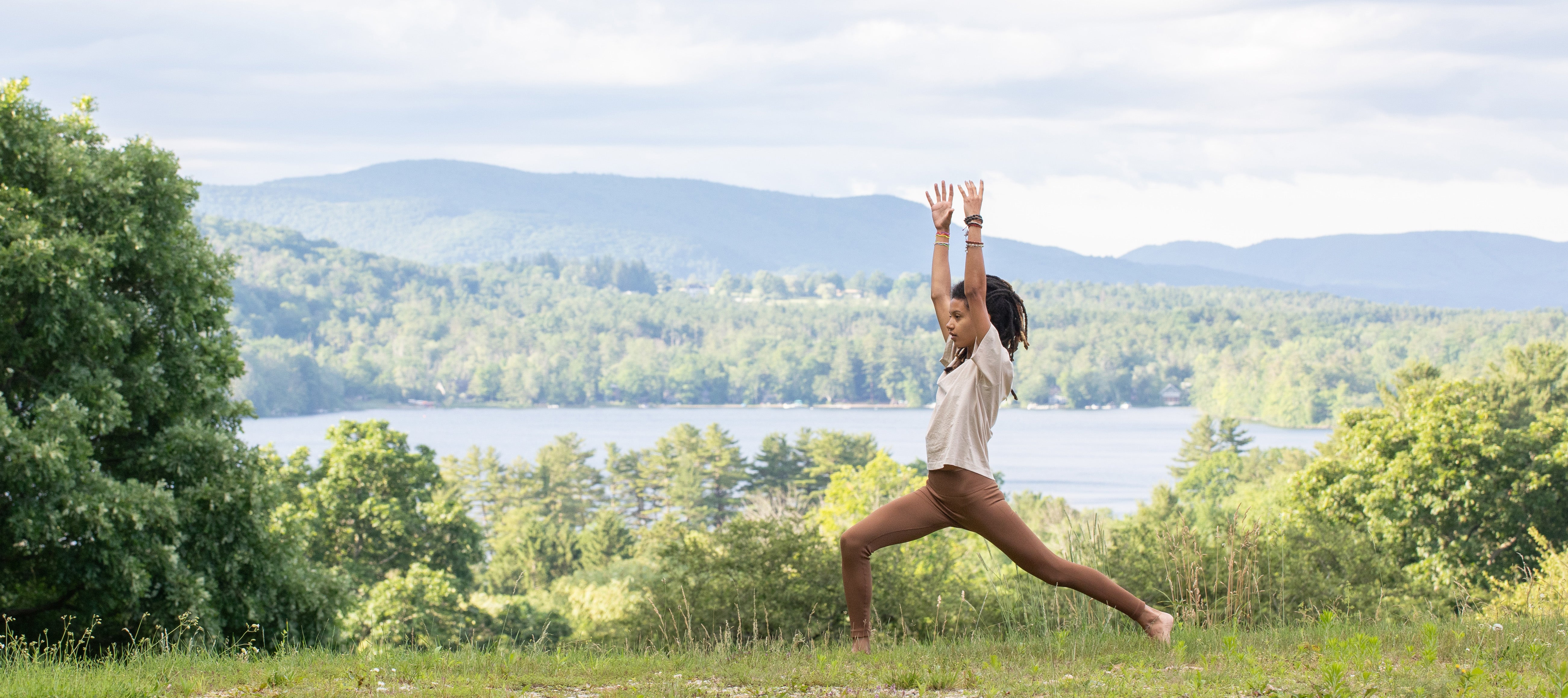 The Sovereign Soul: Walking the Path of Reclamation Woman with hands raised in a yoga pose next to a lake and mountains in the Summer