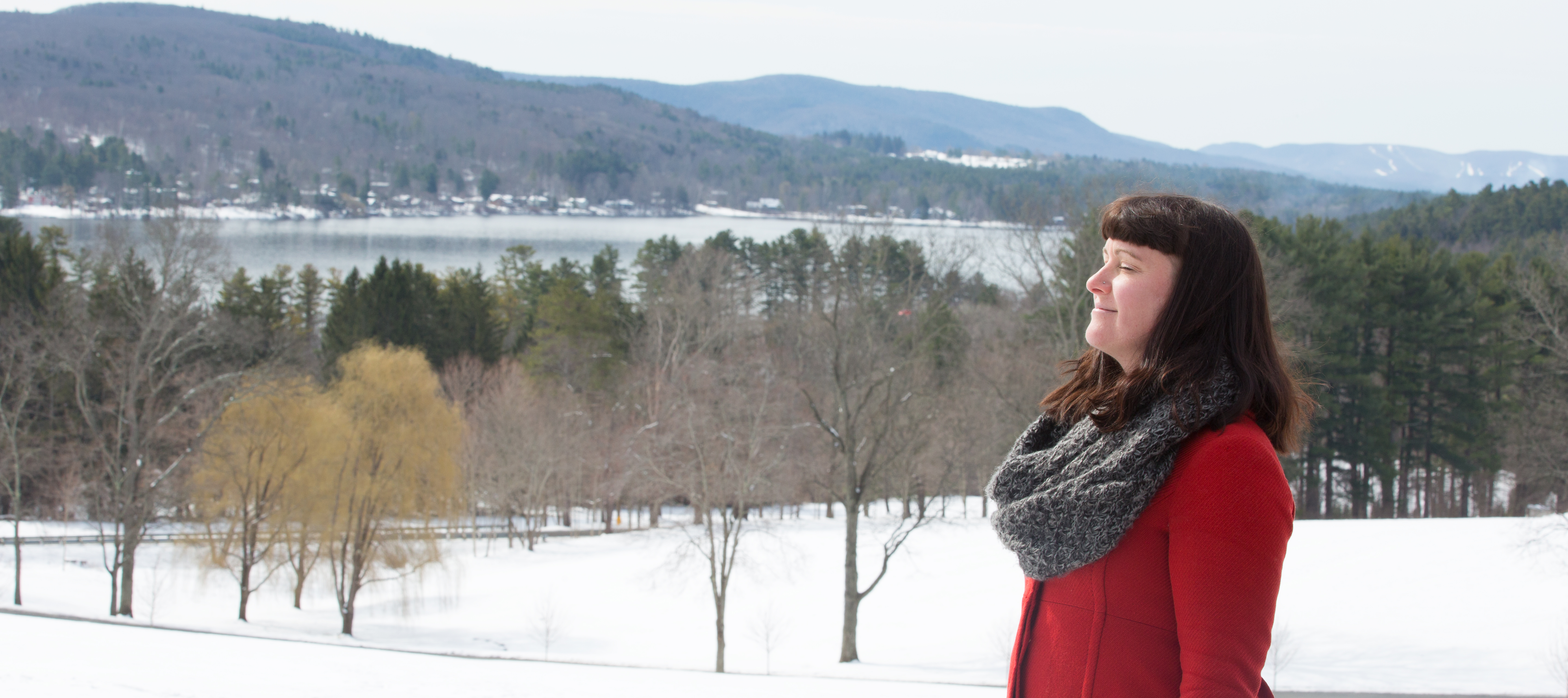 Connect to Your Heart's Longing Woman standing with eyes closed outdoors in the winter with hills and lake in the background.