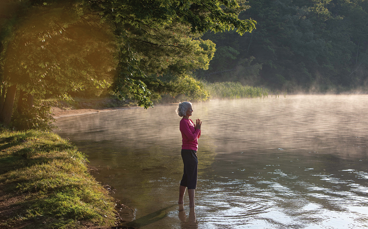 Find Your Escape Woman with hands together standing in a lake.