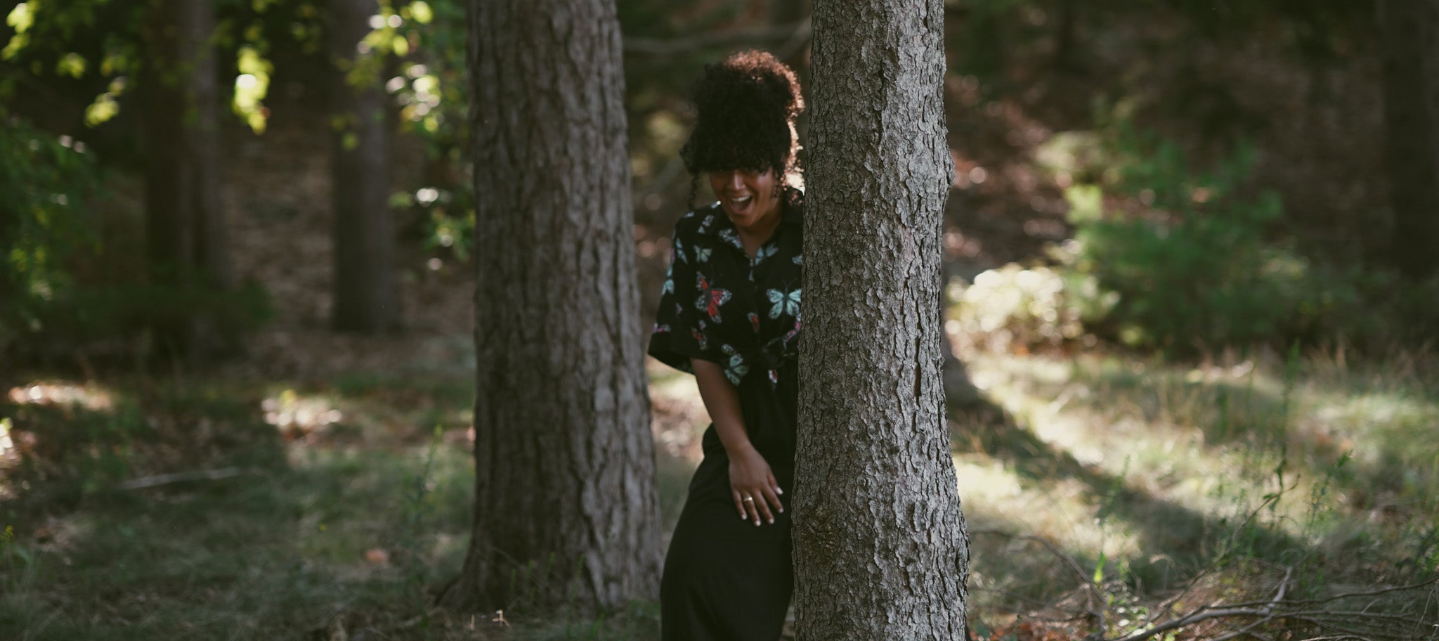 Yera Gomes smiling in the woods between two trees