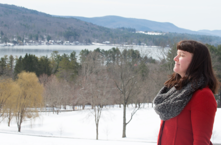 Woman standing with eyes closed outdoors in the winter with hills and lake in the background.