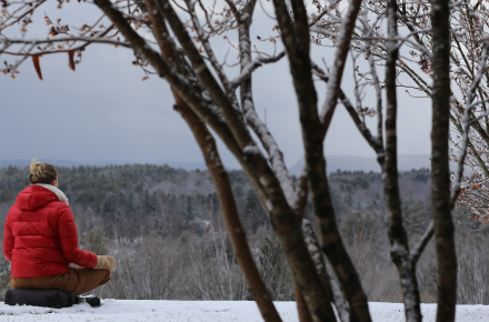 Woman in red jacket sitting on snowy ground looking out at the winter landscape.