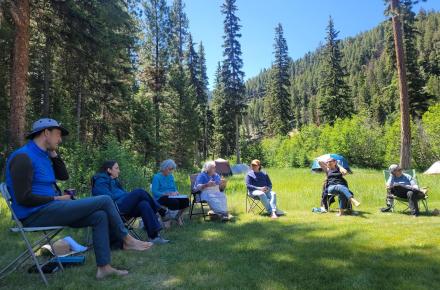 Group of people seated in chairs in a clearing in the woods.