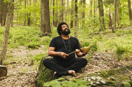 Reggie Hubbard sitting in the forest, smiling, holding a sound bowl