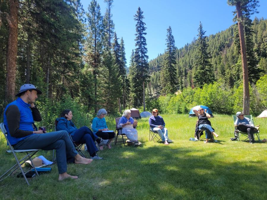 Group of people seated in chairs in a clearing in the woods.