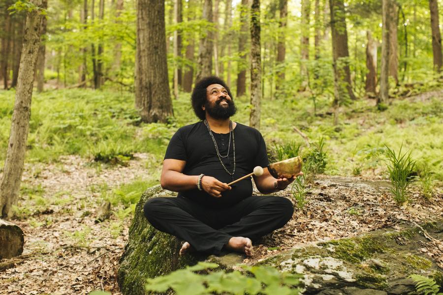 Reggie Hubbard sitting in the forest, smiling, holding a sound bowl